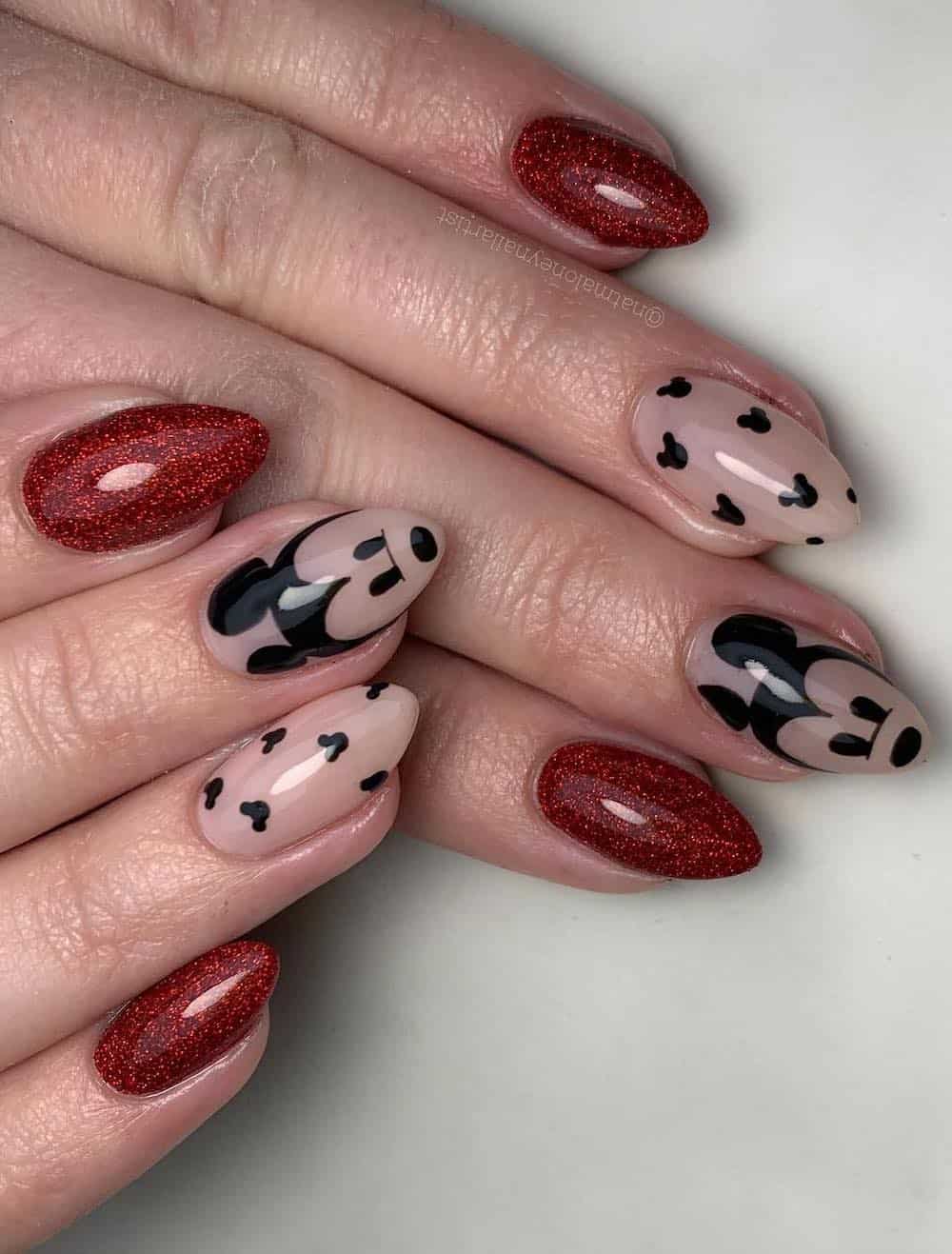 Medium almond nails with a Mickey Mouse design featuring nude polish, glittering red polish, and black nail art