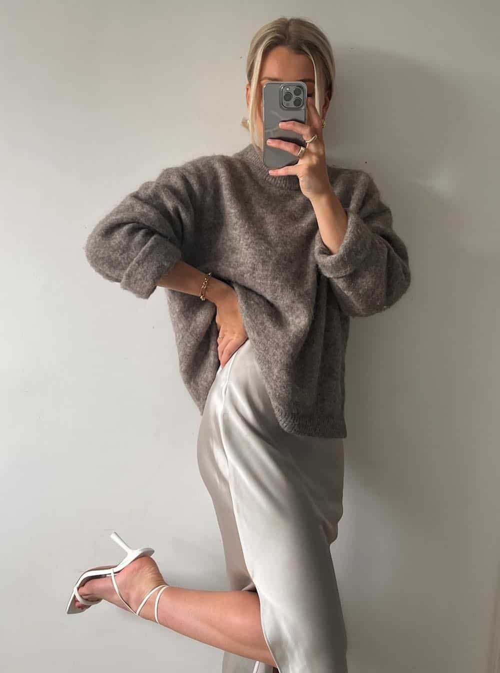Woman wearing a silver slip skirt with a grey sweater and silver heels.