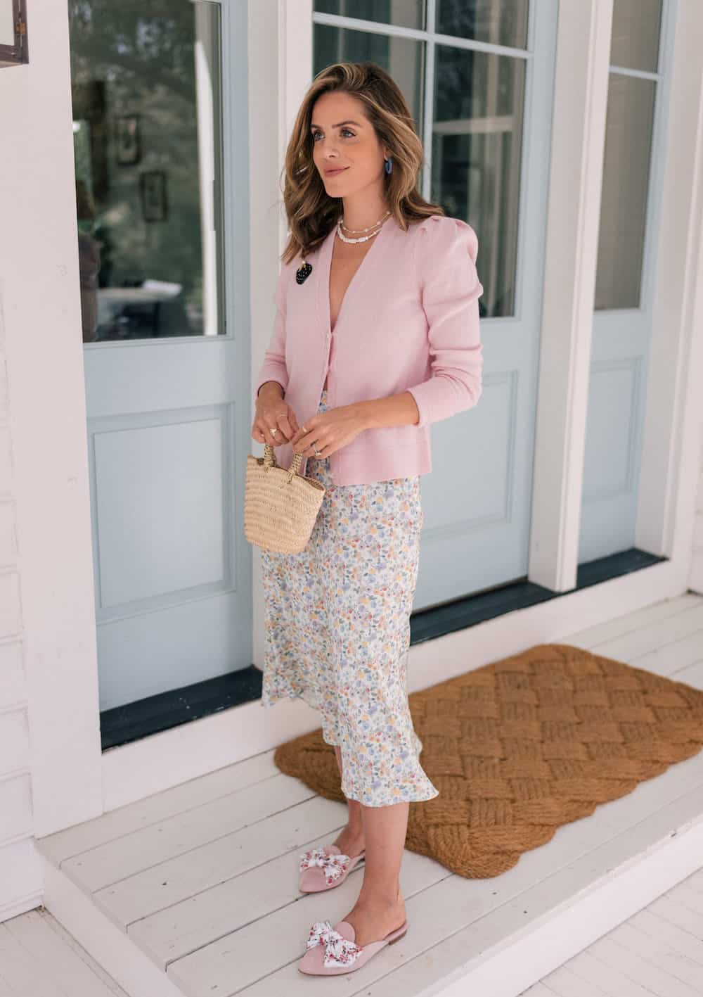 Woman wearing a floral midi skirt, a pastel pink cardigan and pastel pink mules with a floral bow.