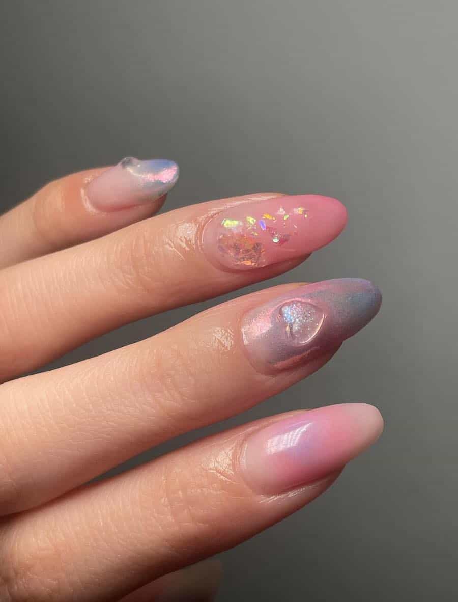 Medium almond nails with pink, purple, and nude polish accented with clear heart gems, and iridescent flakes