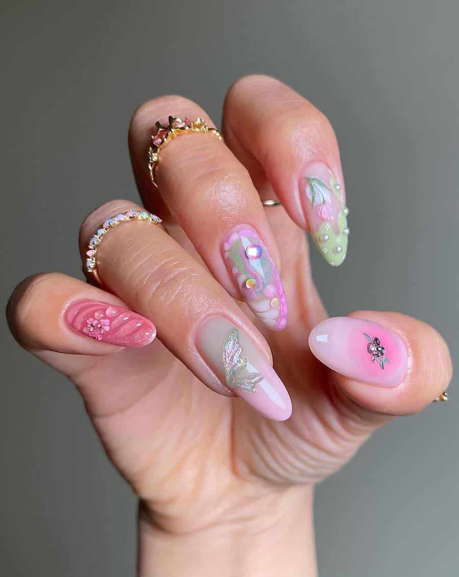 Long almond nails with shades of pink, green, and blue featuring gems, floral art, and fairy wing details