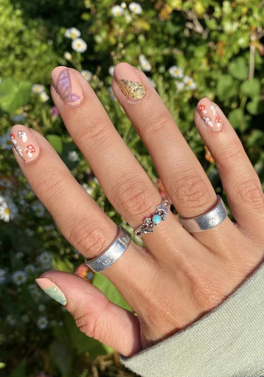Short nude round nails painted in fairy core nail art including mushrooms and wings with gold foil accents