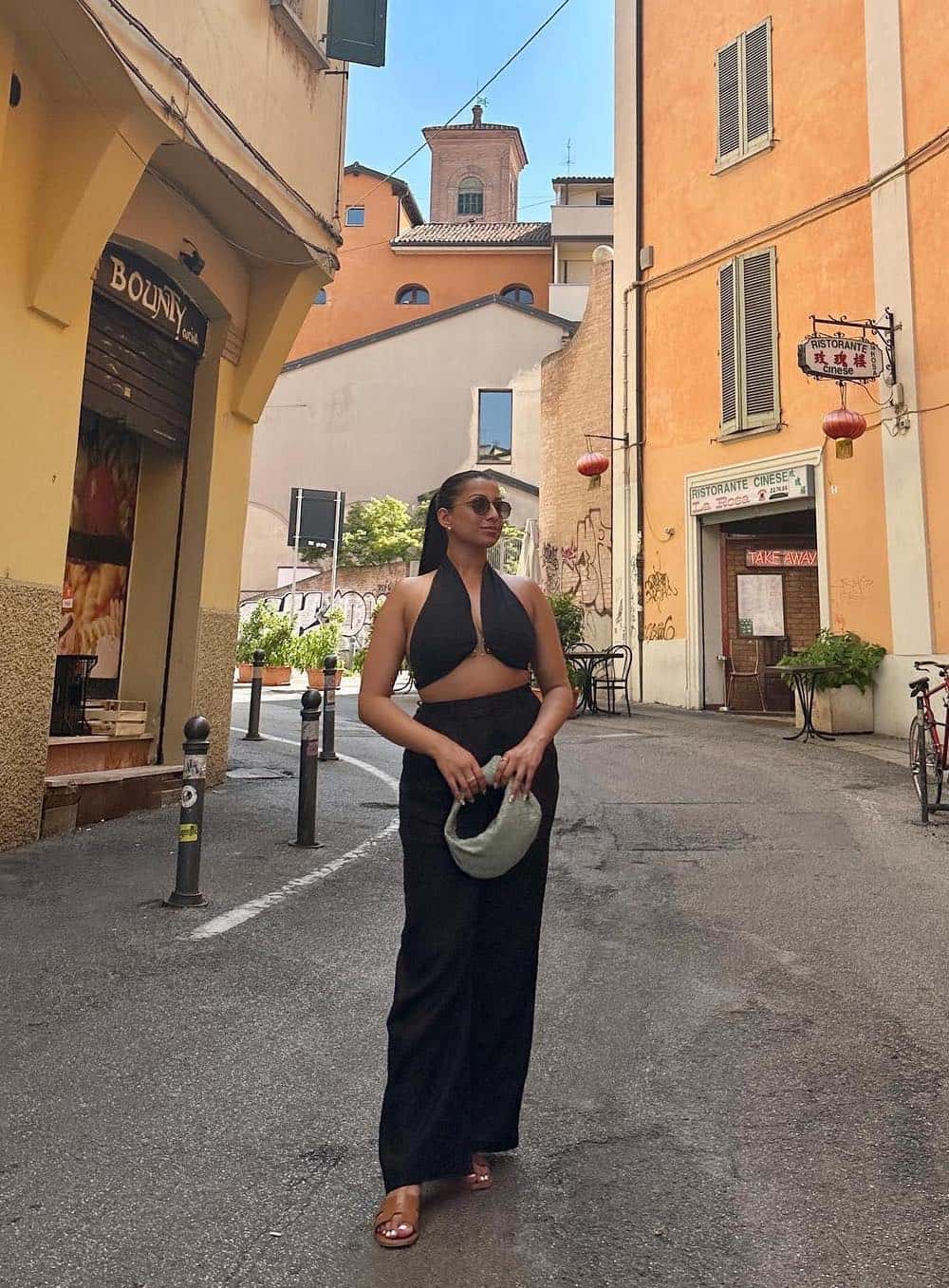 Woman wearing a long black skirt and crop top with brown sandals in Italy.