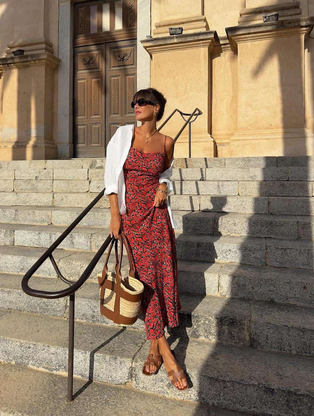 Woman wearing a red floral printed midi dress with brown sandals and a rattan bag.