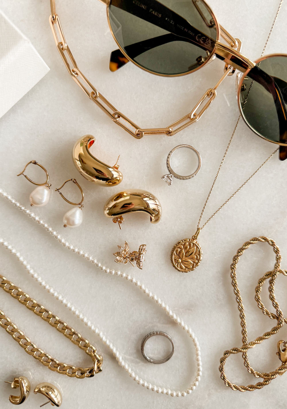 image of a minimal collection of jewelry on a marble board including gold earrings, chain necklaces, pearl earrings, and a pearl necklace