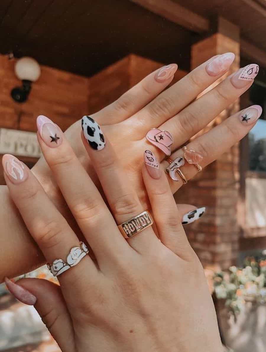 Medium almond nails with pink, white, and black designs featuring Western-inspired designs like paisley, cow print, and stars