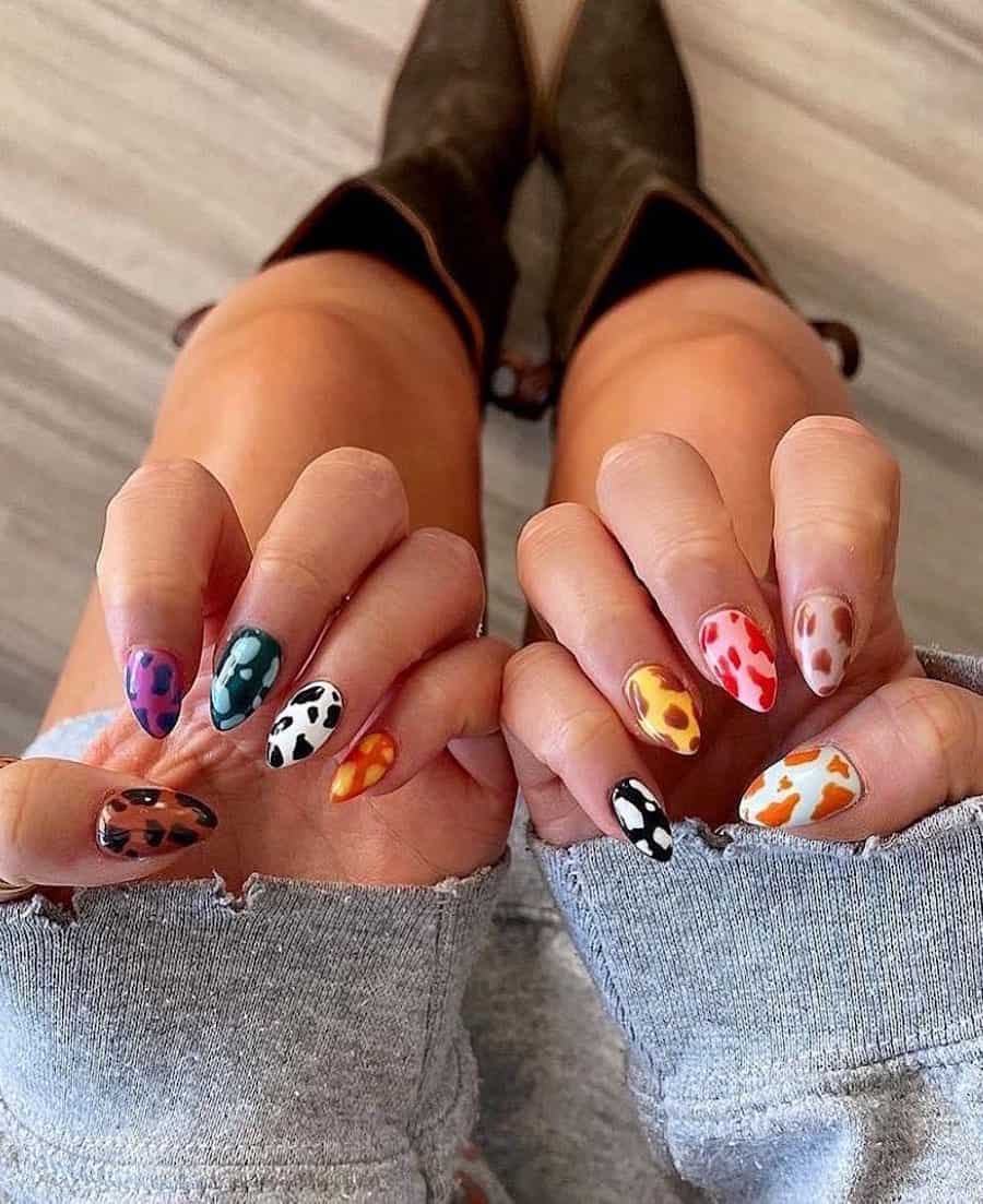 Medium almond nails painted in cow print patterns with multiple colors