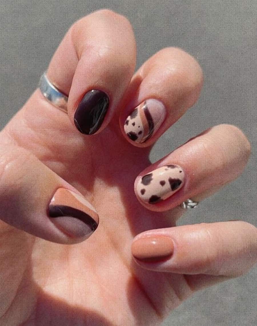 Short round nails painted with beige and brown polish featuring cow print and waves