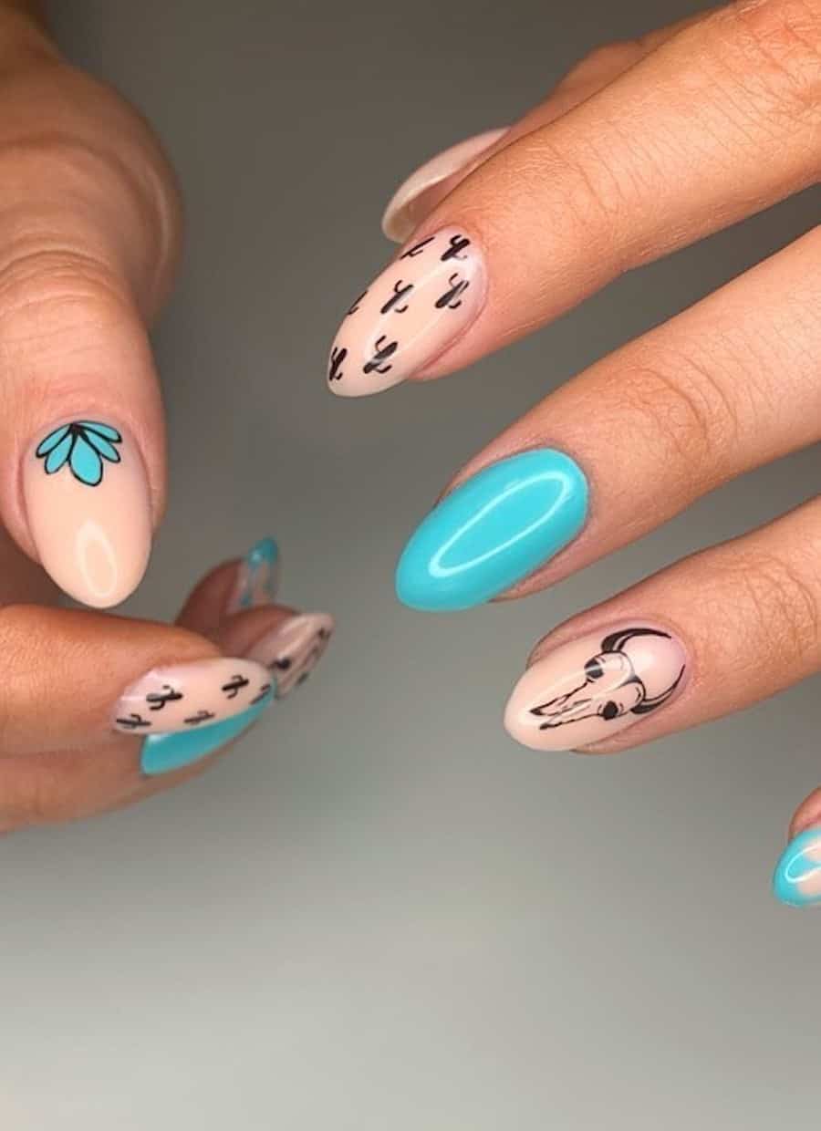 Medium almond nails painted in bright blue and nude polish featuring Western cactus and skull designs