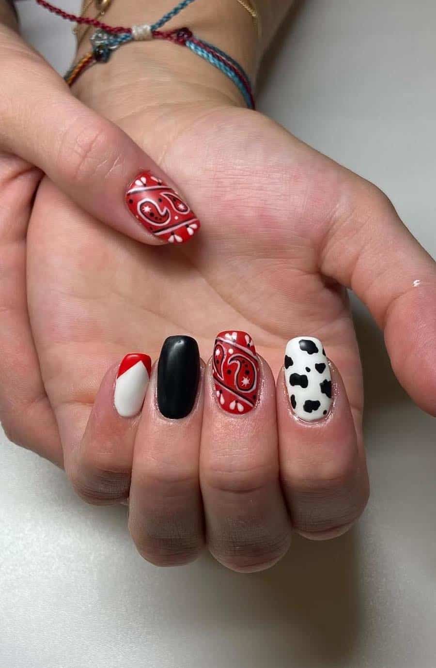Short squoval nails featuring red, white, and black designs like paisley and cow print