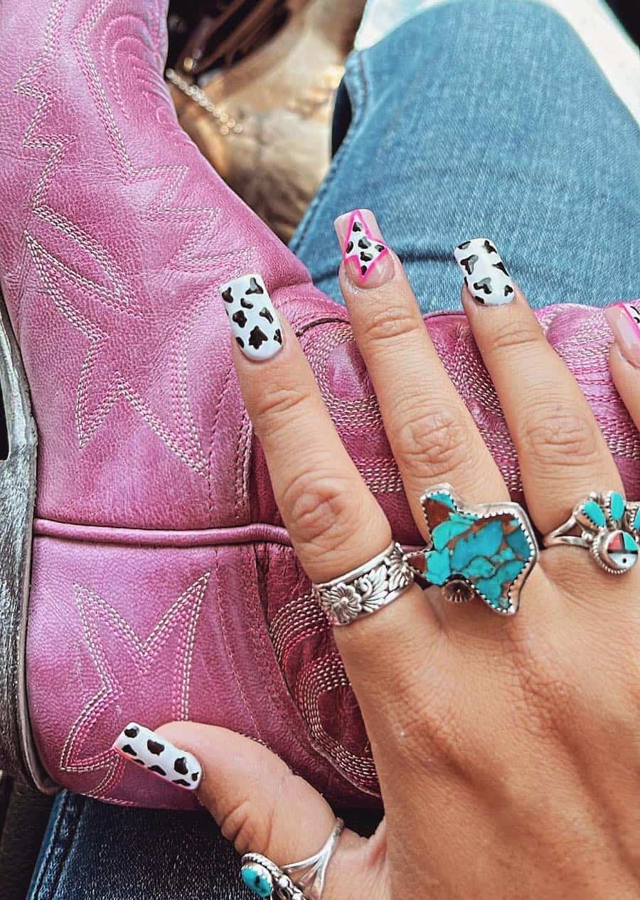 Medium square nails painted with a cow print design and a pink lightning bolt