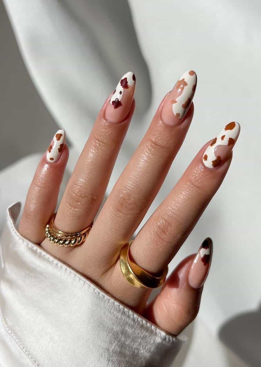 Long almond nails featuring wavy white tips with brown ombre cow print