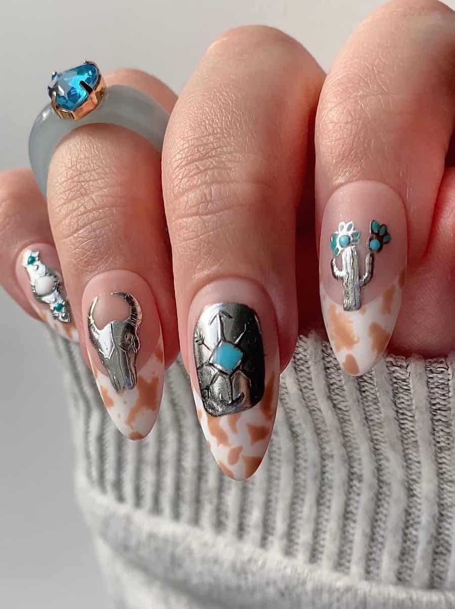 Long nude almond nails featuring light brown cow print tips and silver and teal Western nail art