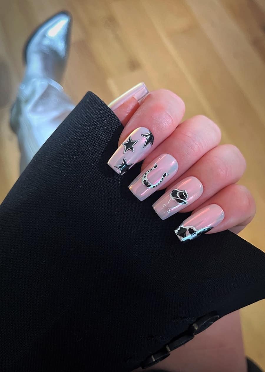 Long coffin nails painted a soft pink chrome with silver and black Western-inspired designs