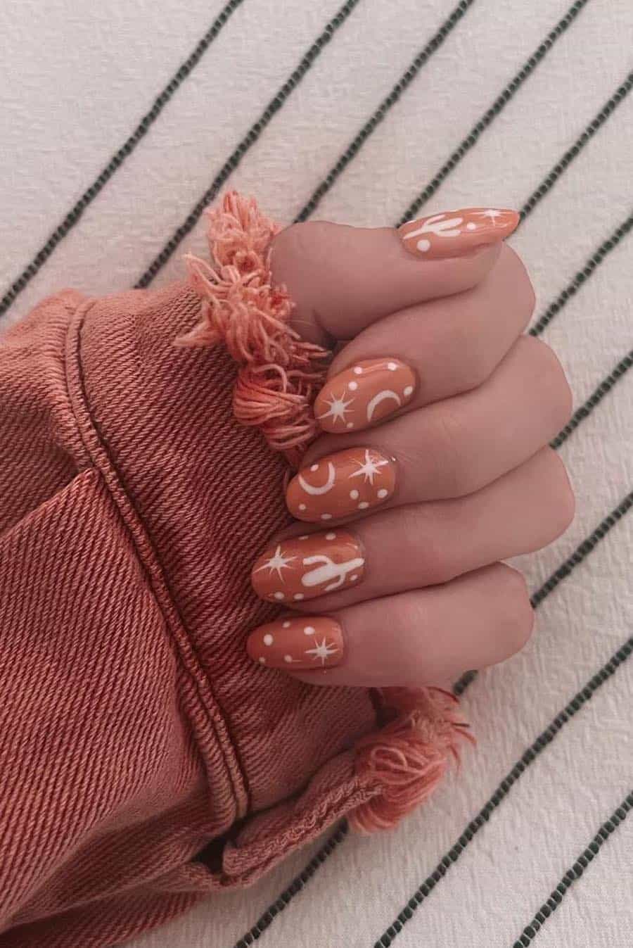 Medium round nails with dusty orange polish and white Western-inspired nail art