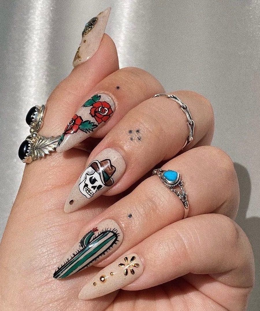 Long almond nails painted a beige polish with Western-themed nail art like cactus, skulls, roses, and cowboy hats