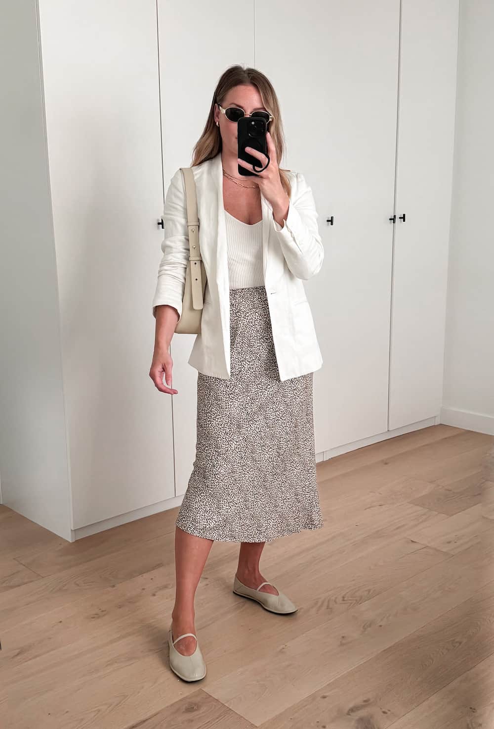 Christal wearing a patterned slip skirt, ballet flats, a white tank top and a white blazer.