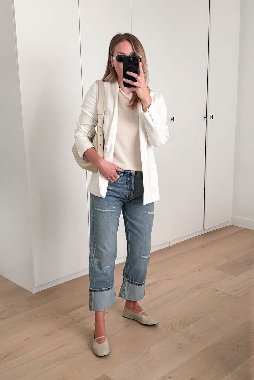 Christal wearing jeans, ballet flats, a white knot top and a white blazer.