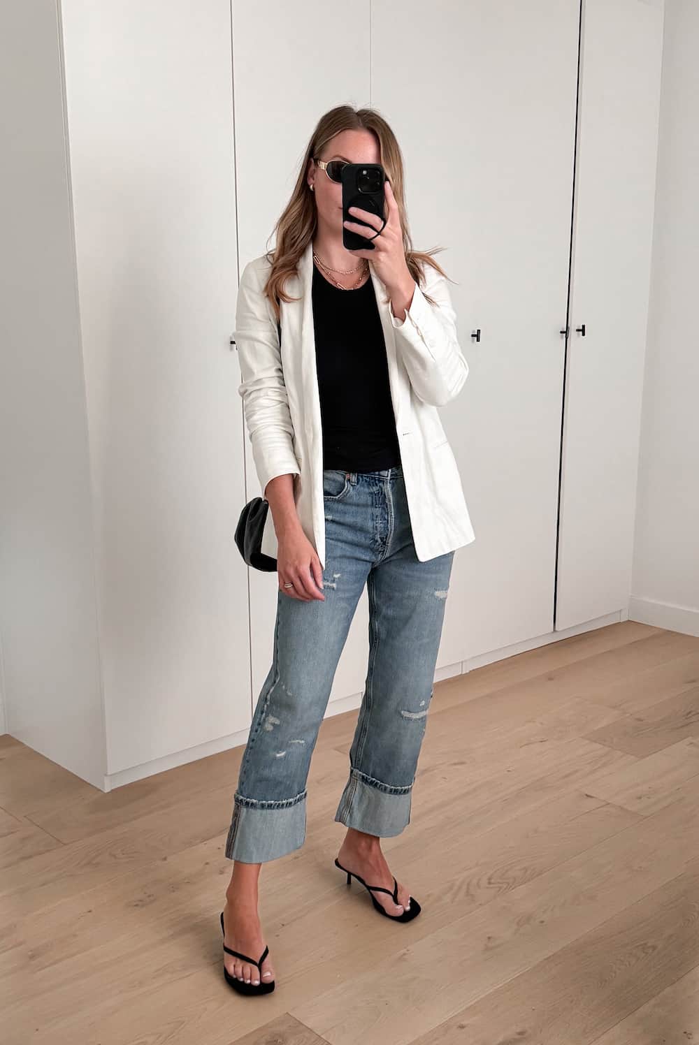 Christal wearing jeans, black heeled sandals, a white blazer and a black knit top.