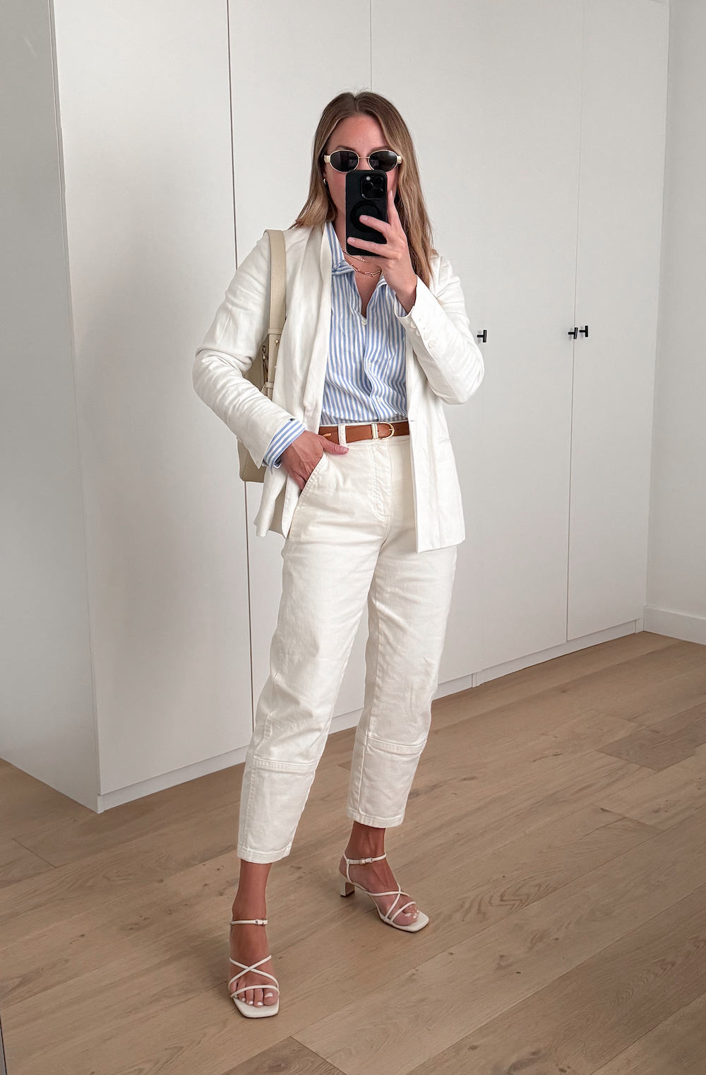 Christal wearing white cargo pants, a blue and white striped button down, a white blazer and white heeled sandals.