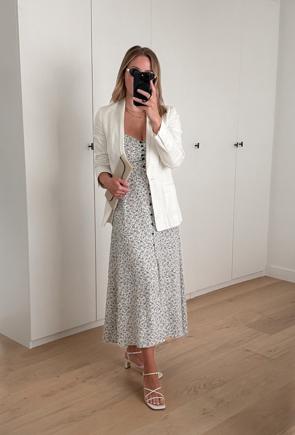 Christal wearing a floral printed sundress with white heeled sandals and a white blazer.