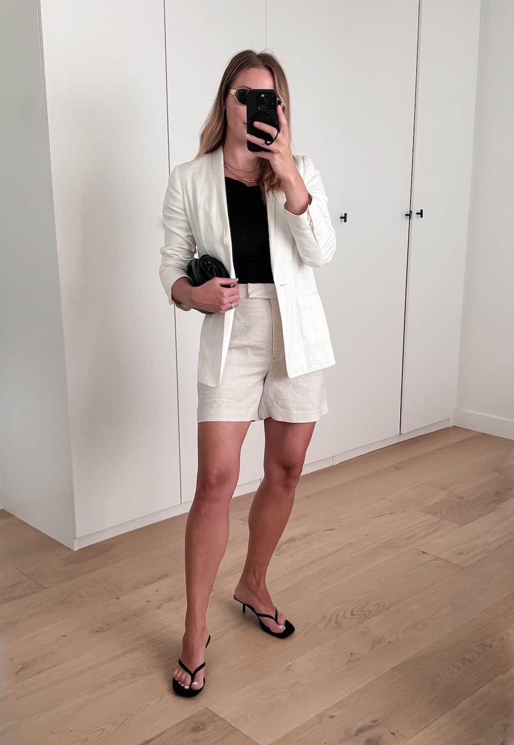 Christal wearing cream shorts, a black knit top, a white blazer and black heeled sandals.
