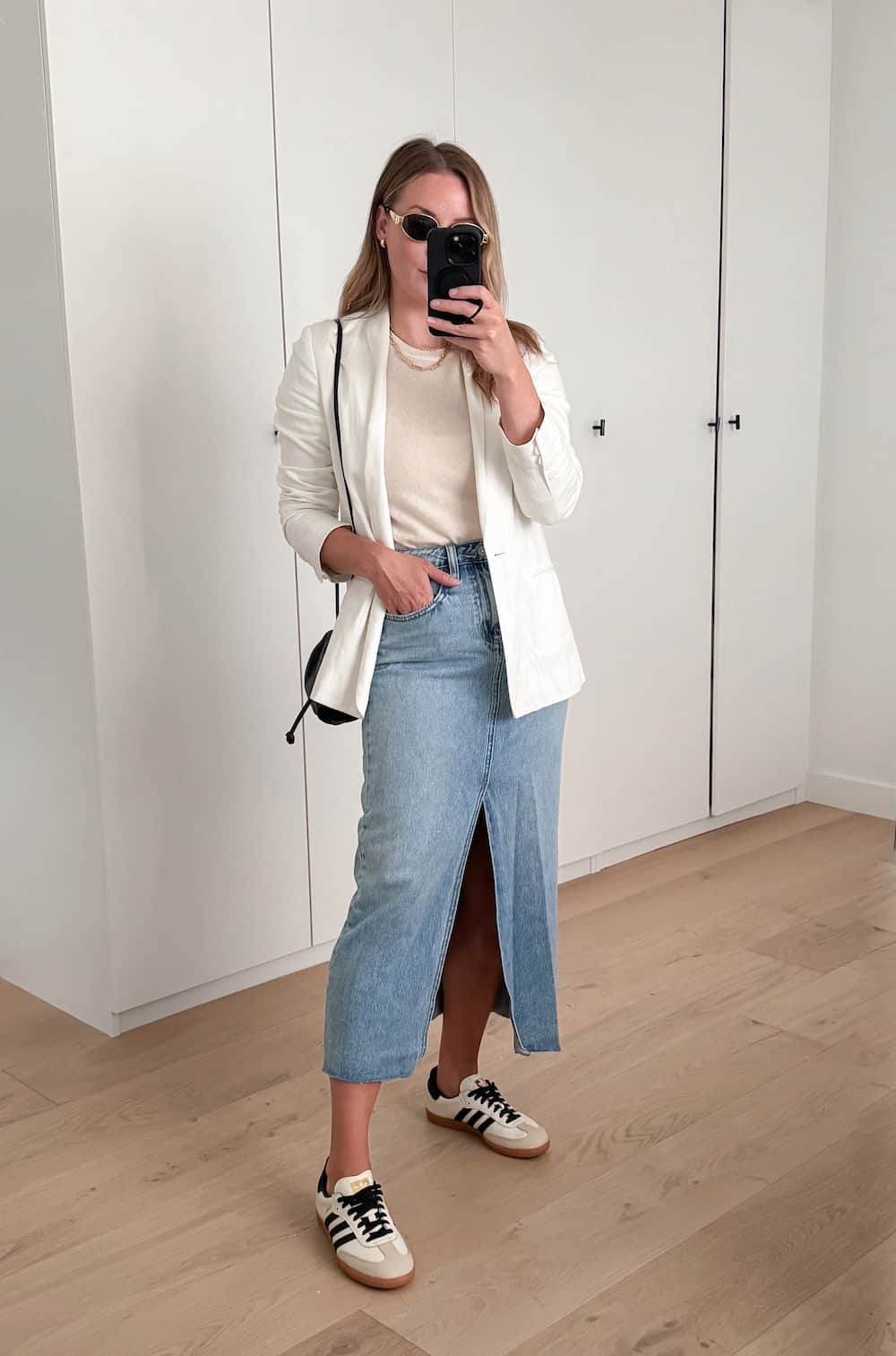 Christal wearing a denim midi skirt, a cream sweater, sneakers and a white blazer.