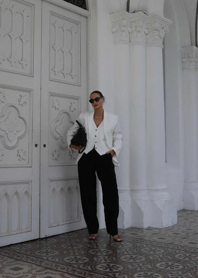 woman wearing an oversized white blazer over a white waistcoat with black trousers 