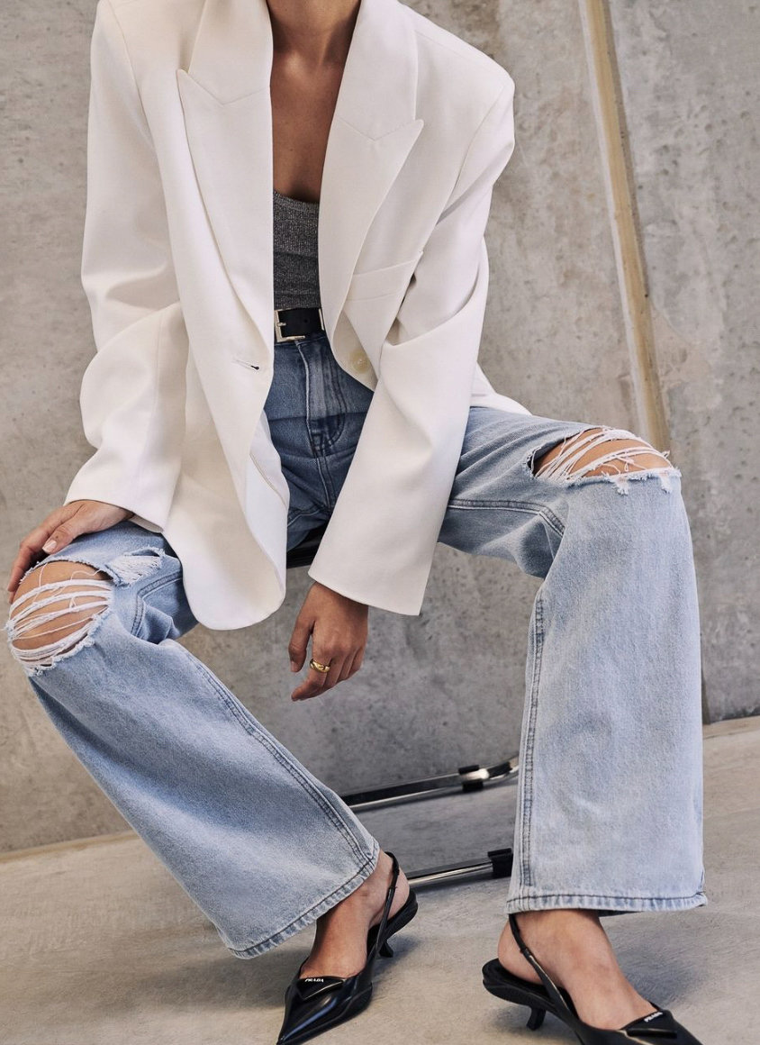 woman wearing an oversized white blazer with ripped blue jeans and black kitten heel slingbacks