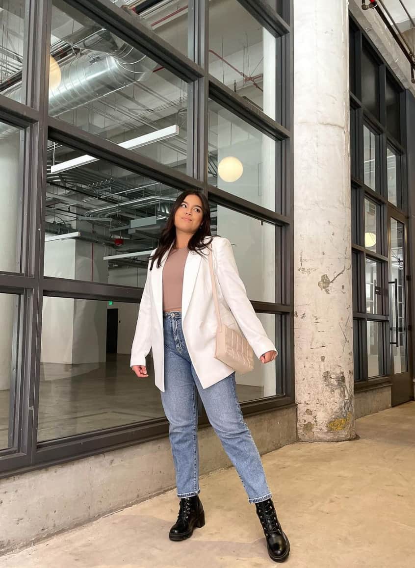 woman wearing a white blazer over a nude bodysuit with blue jeans and black combat boots