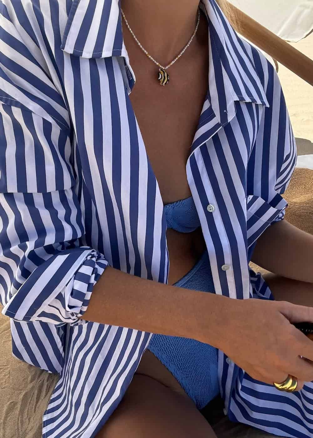 a woman wearing a blue bikini and an oversized striped blue and white button-up