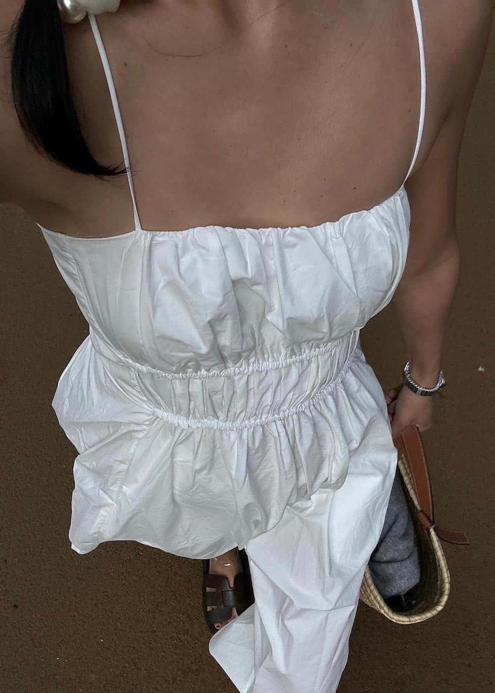 an overhead shot of a woman wearing a white summer dress with strappy slides and a woven tote