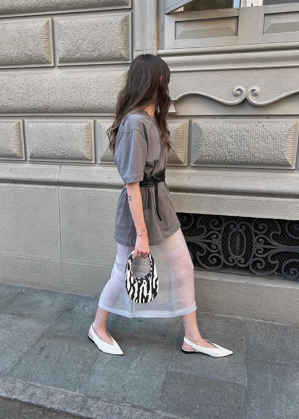 a woman wearing a sheer white midi skirt with a belted grey tee and white slingback flats