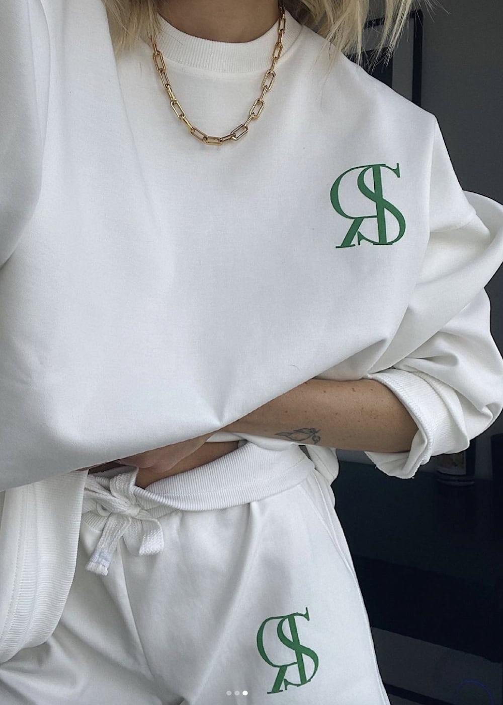 an up-close shot of a woman wearing a matching white sports sweat set with green monogrammed letters