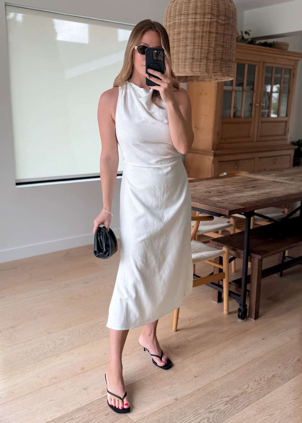 a woman wearing a white midi dress with strappy black heels and a black clutch