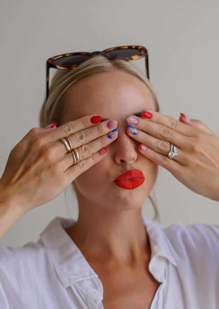 a woman with short stiletto nails featuring red solid-colored nails and red French tips with blue star accent nails and floral accent nails