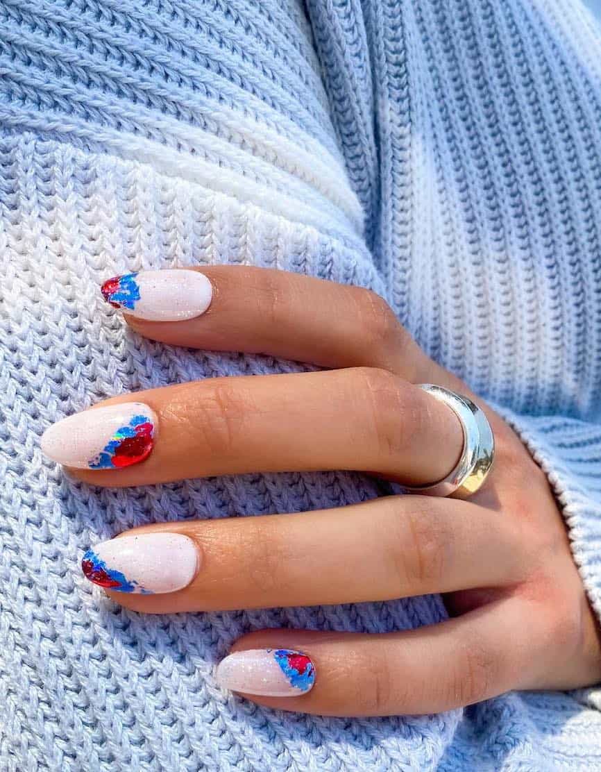 short white almond nails with a glitter topcoat and metallic red and blue foil accents