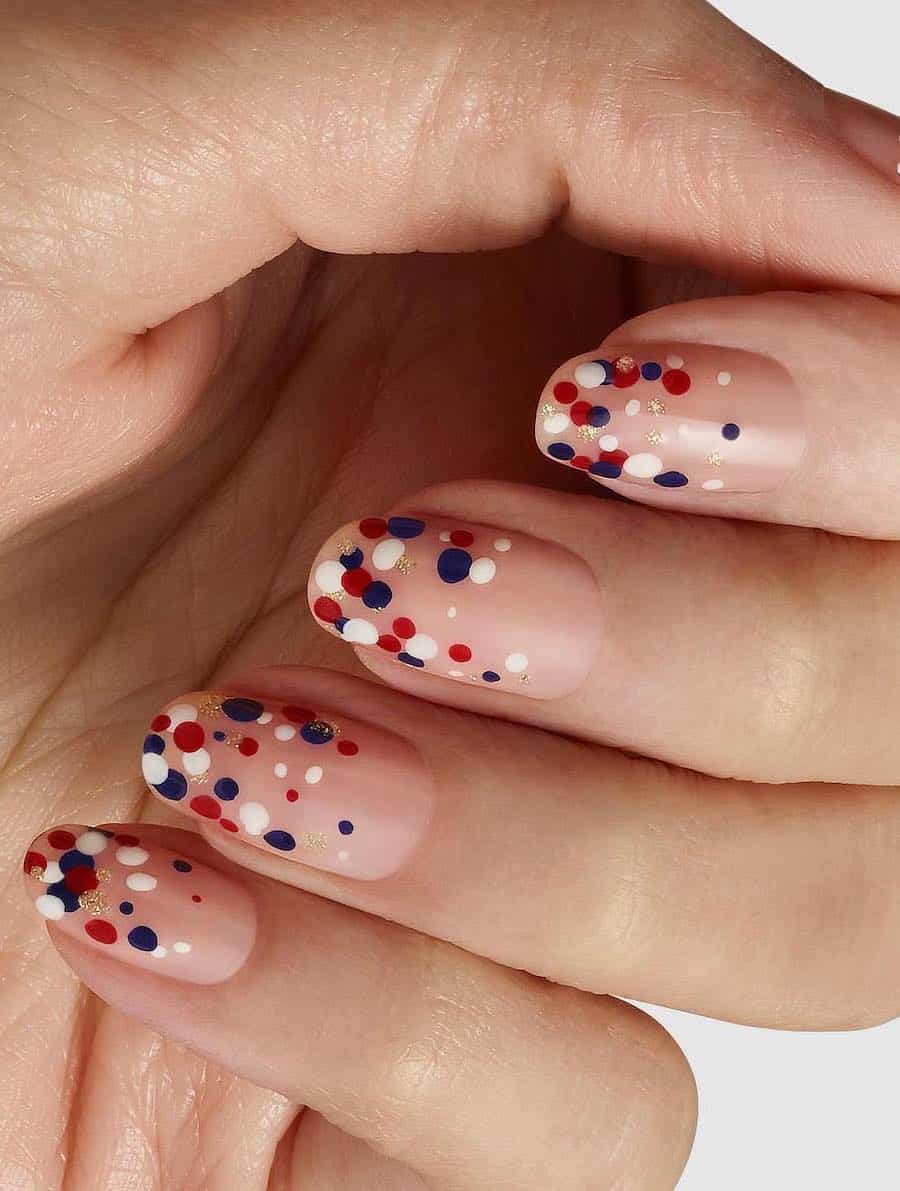 short round nude nails with red, white, blue, and gold glitter dots