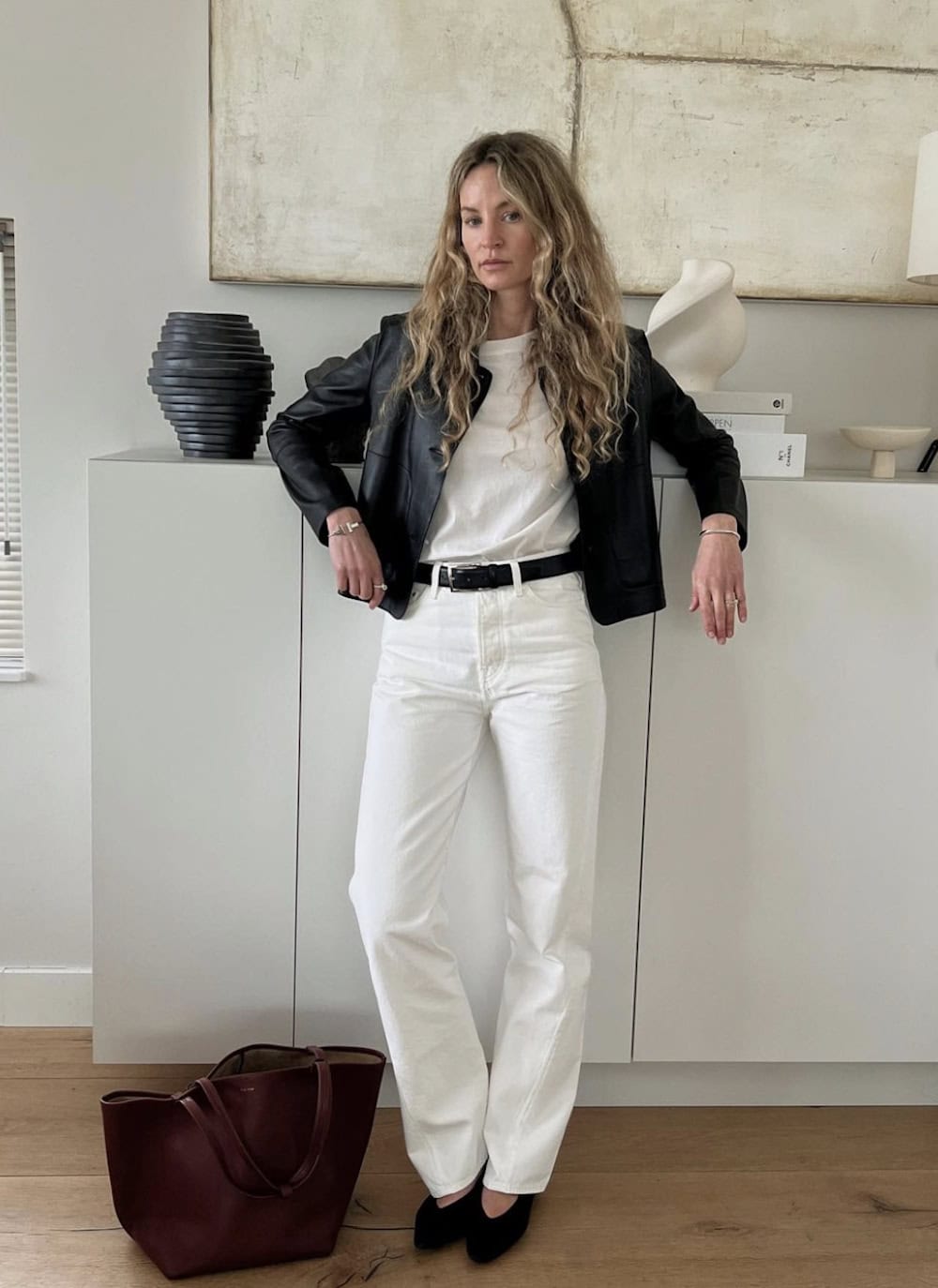 Woman wearing white jeans, black pumps, a white t-shirt and a black leather jacket.