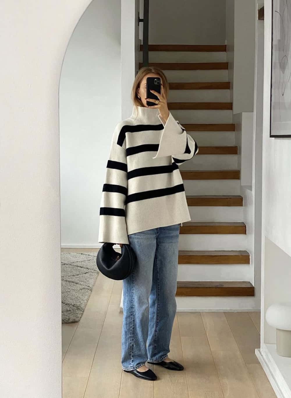 Woman wearing baggy jeans, a black and white striped baggy sweater and black ballet flats.