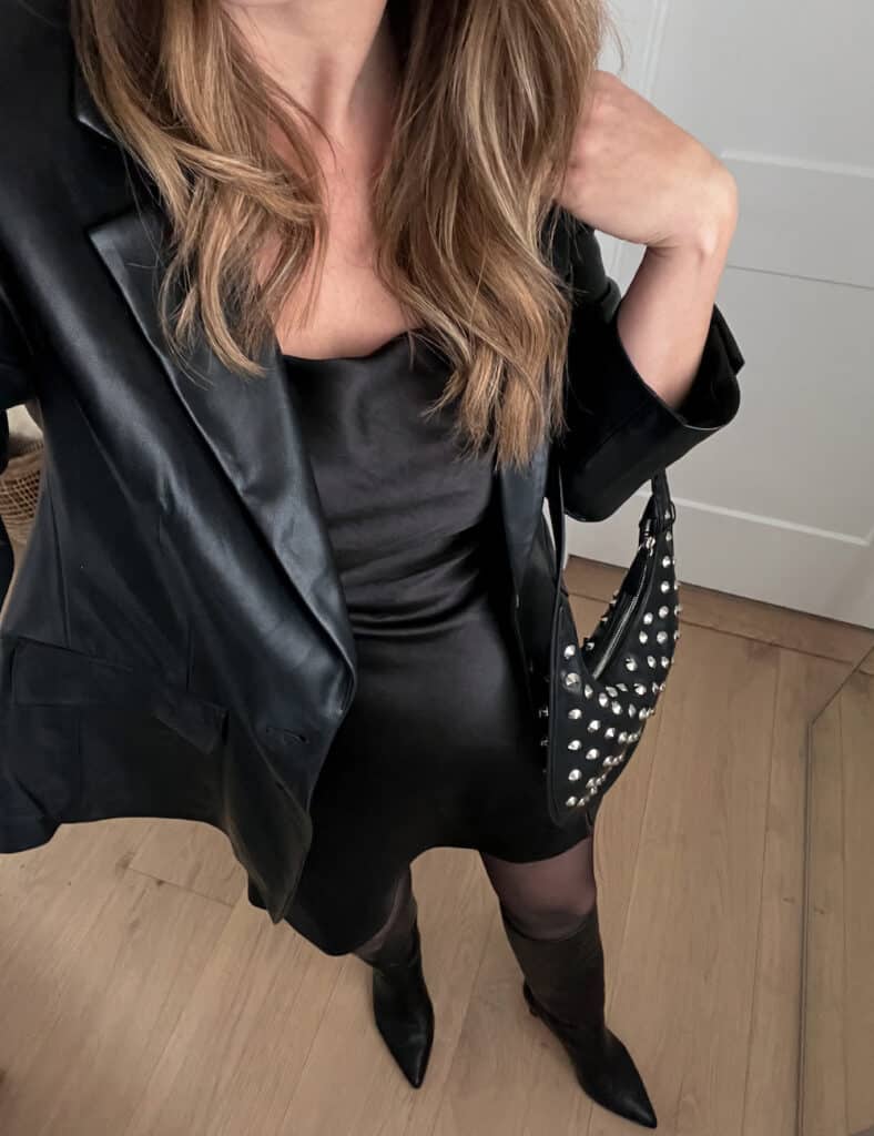 woman wearing a black mini slip dress with a black leather blazer, sheer black rights and black knee high boots