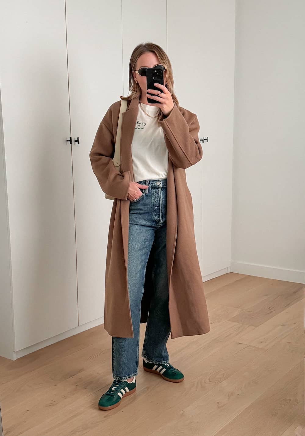 Christal wearing jeans, a white tee, a brown duster coat and green sneakers.