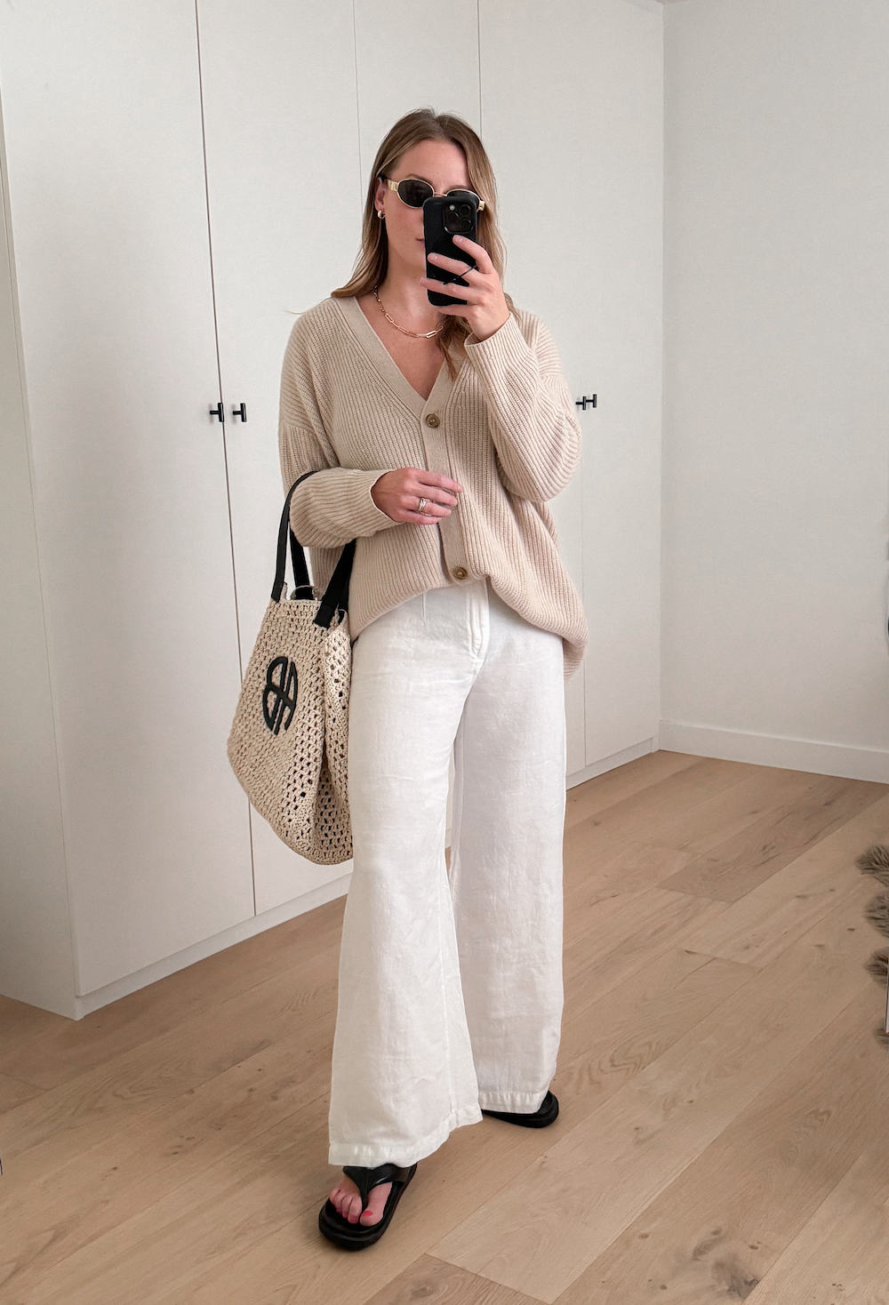 Christal wearing linen pants and an oversized cardigan with a straw bag and black flip flops.