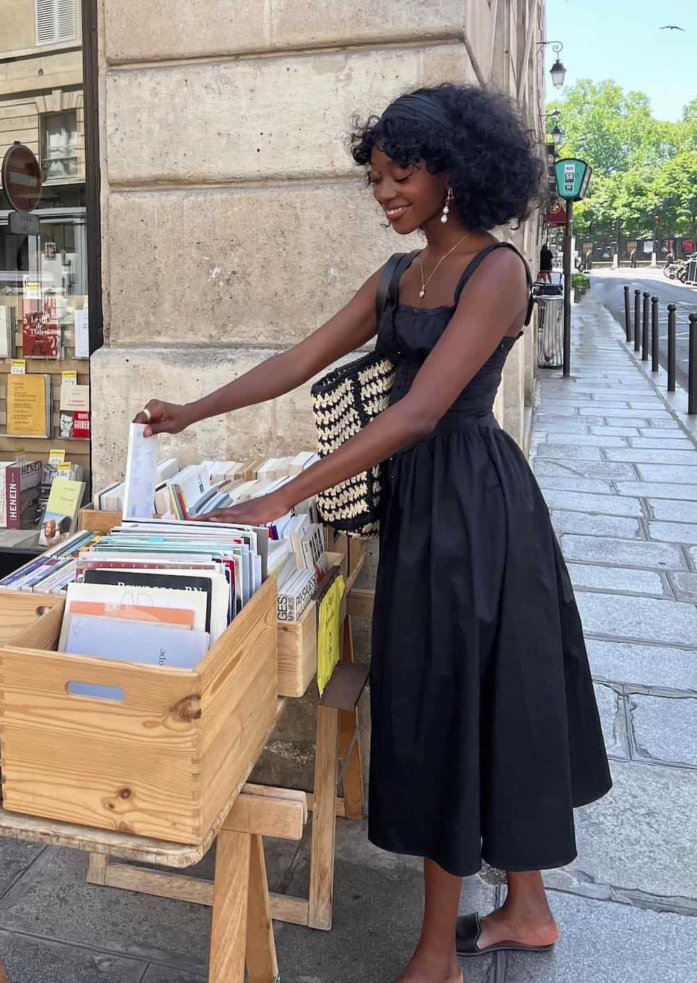 Woman wearing a black sundress with black sandals while attending an outdoor market.