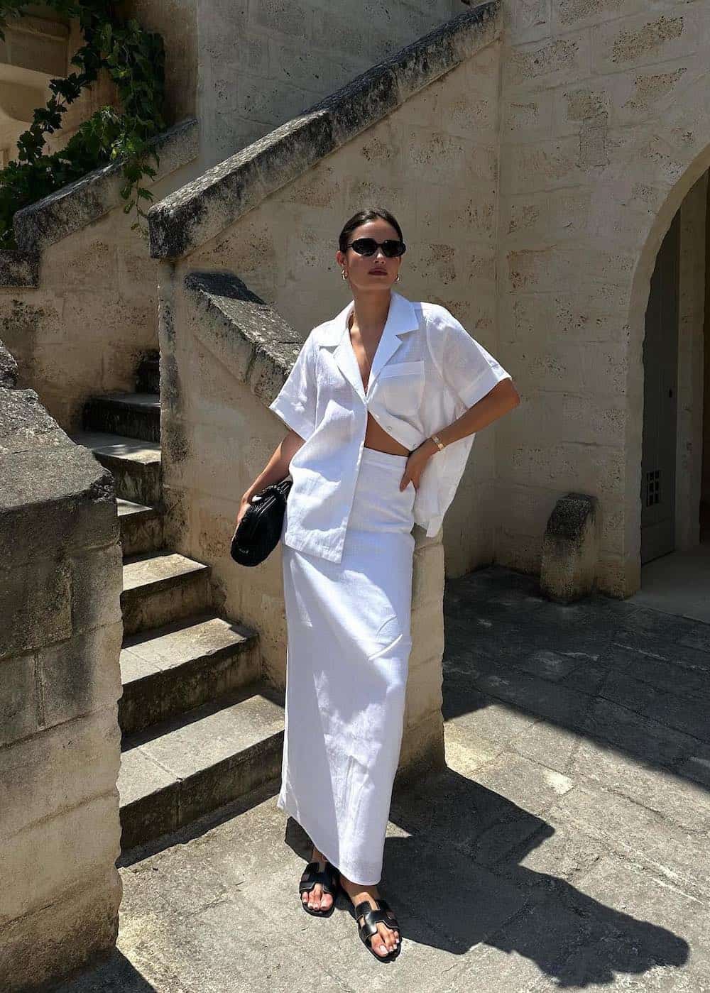 Woman wearing a white linen shirt and maxi skirt set with black sandals.