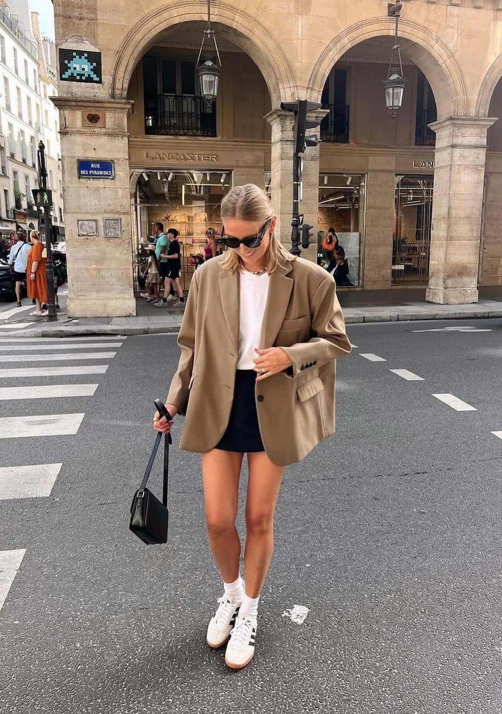Woman walking in the street wearing a black skirt, a white t-shirt and an oversized blazer with sneakers.