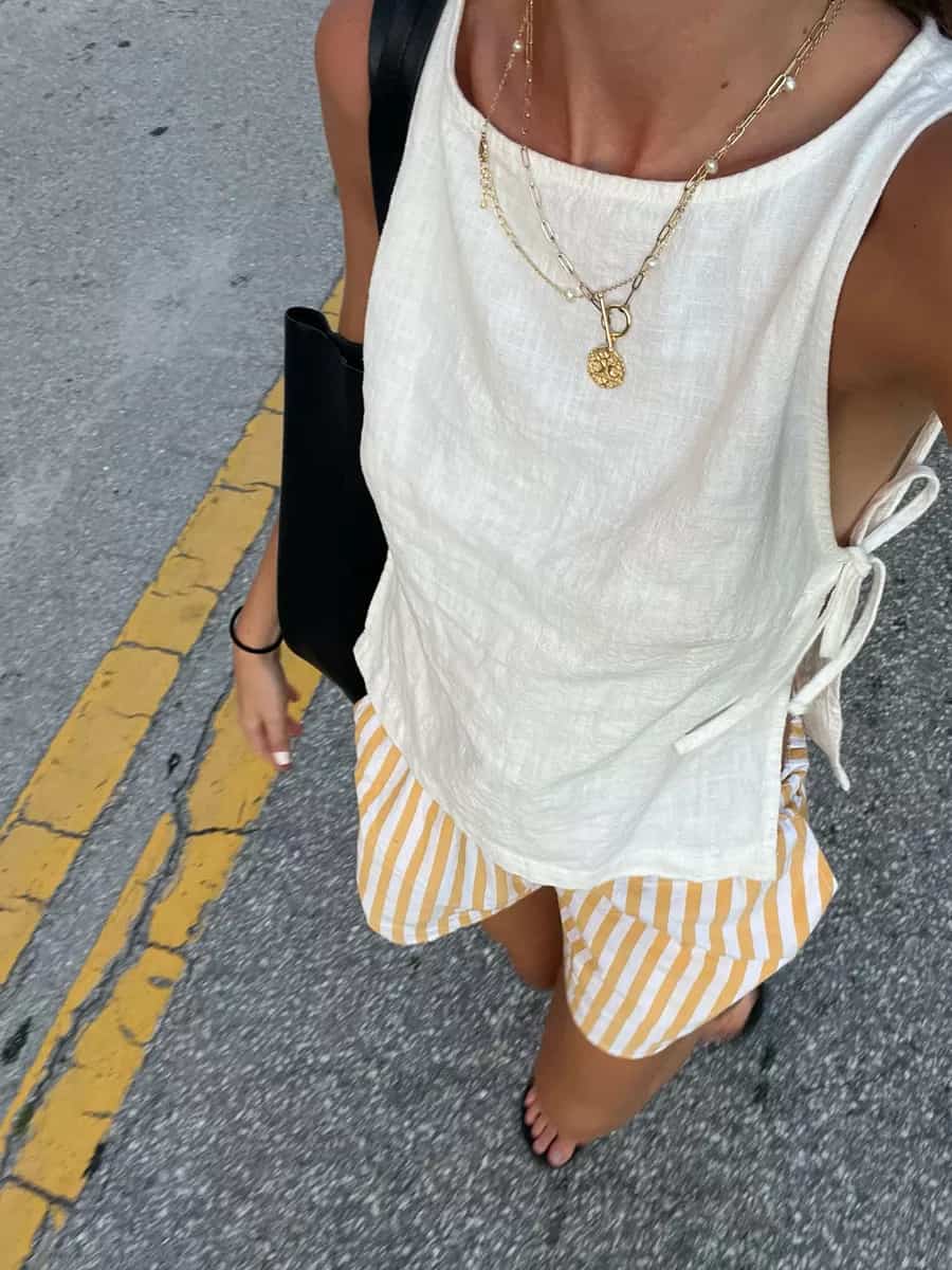 Woman wearing striped linen shorts and a linen tank top with gold accessories.