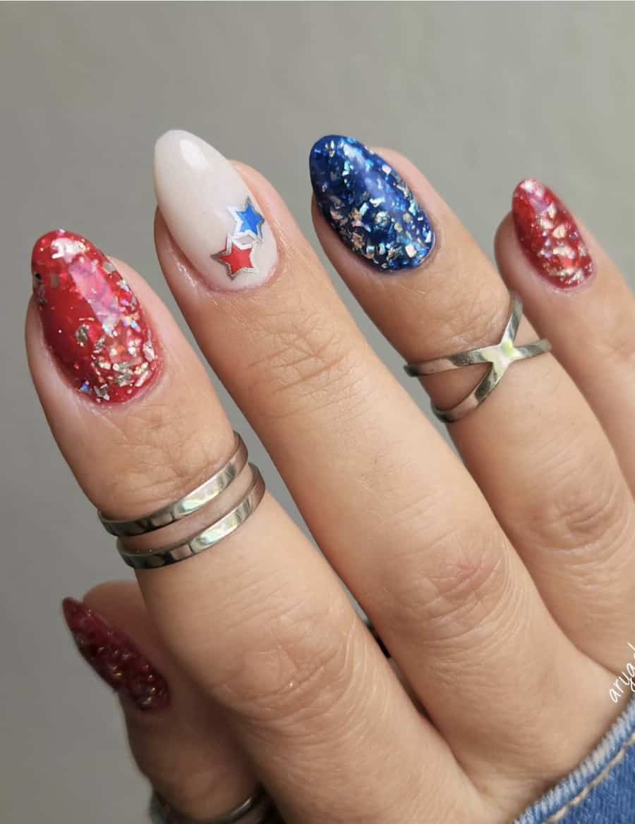 short almond nails with red and blue polish with chunky silver glitter and a milky white accent nail with stars