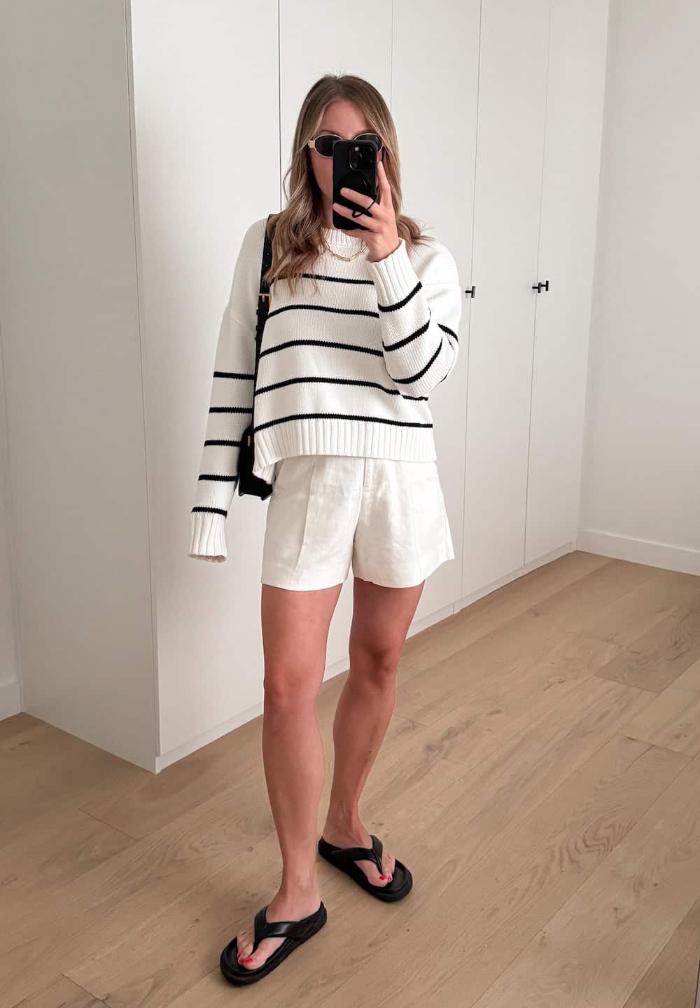 woman wearing a summer outfit with a striped cotton sweater, off-white linen pleated shorts and black chunky sandals