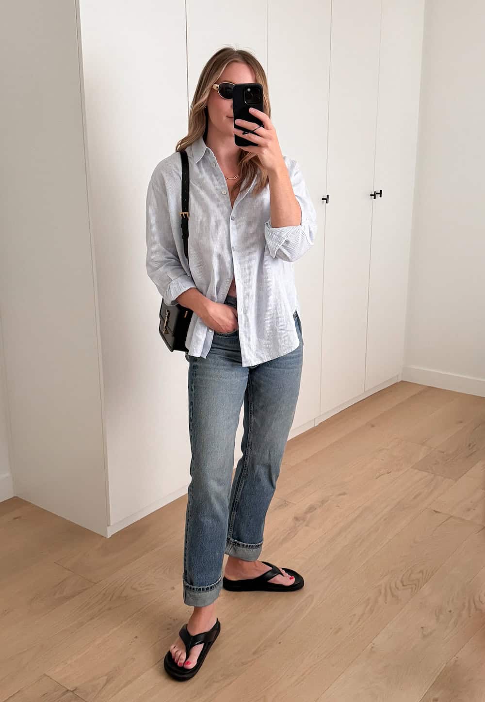 woman wearing a summer outfit with a blue striped button-up shirt, blue jeans, and black chunky sandals